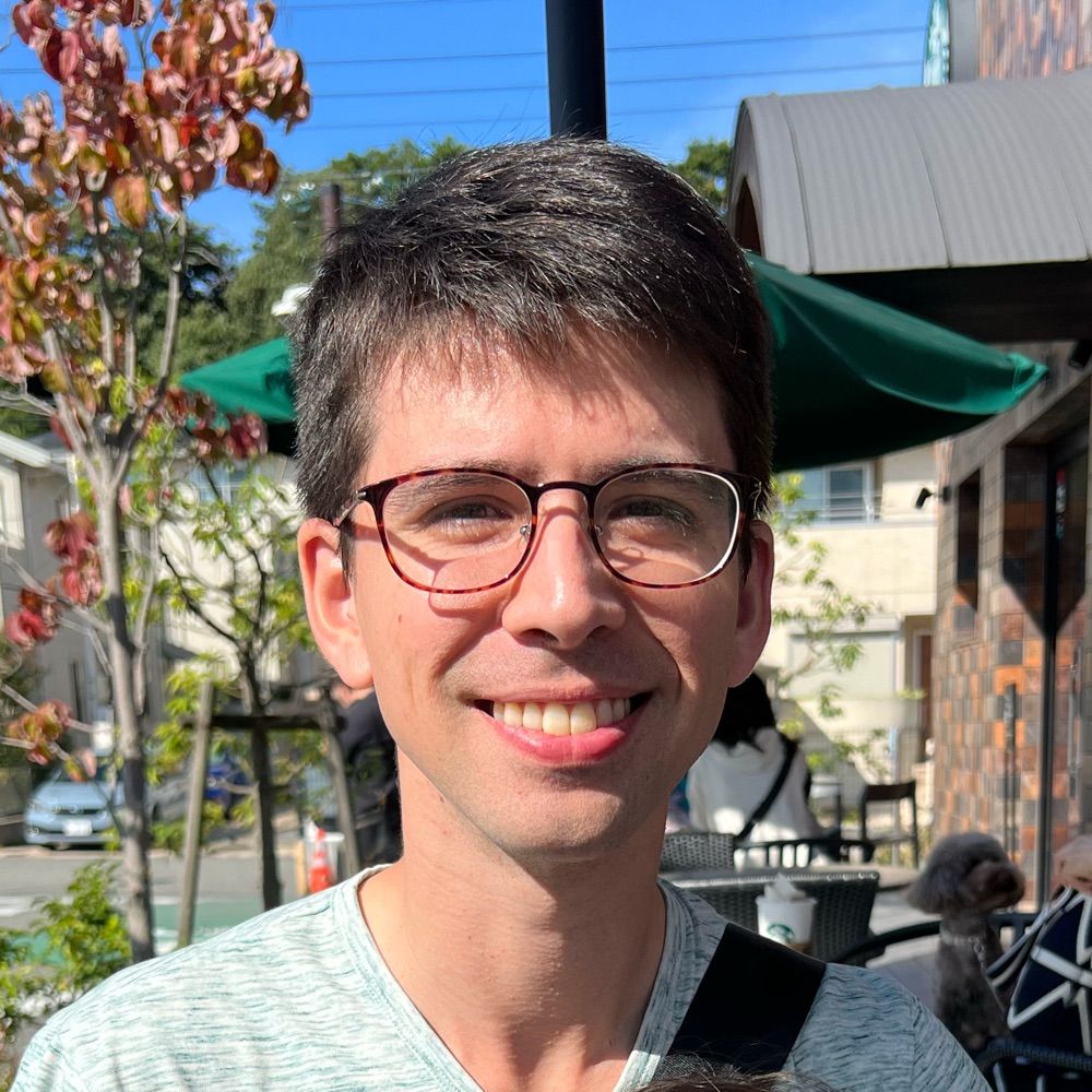 A photo of me sitting at an outdoor terrace smiling and trying to keep my eyes open in the bright sunlight.